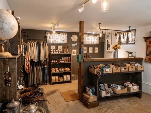 Inside the Bat Cave Road Farm thrift shop in Old Fort, NC — vintage clothing racks, depression glass, cast iron cookware, vinyl records, graphic tees, and antique housewares on hardwood floors with a rustic checkout counter